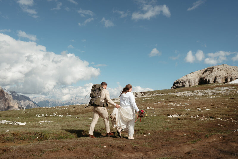 Groom holds brides dress as she hikes and holds her Dolomites florist bouquet during their dolomites elopement 