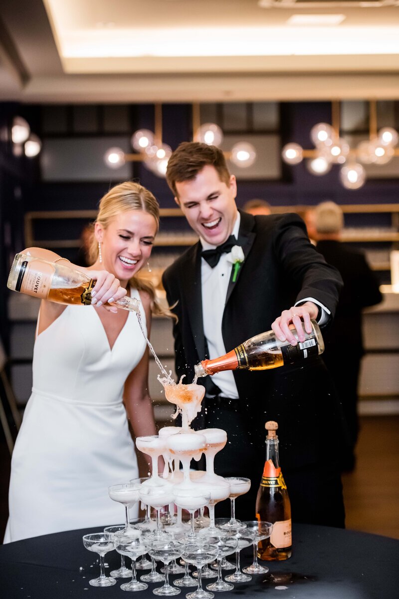 Captured in vibrant detail, this image showcases Kelly and Matthew laughing joyously as they pour champagne into a glittering tower during their lively wedding reception at Hotel Covington, Cincinnati. Their happiness and the sparkling elegance of the champagne tower exemplify the festive spirit of their special day. Perfect for couples seeking inspiration for their own celebration, this photograph highlights a timeless wedding tradition infused with modern charm and excitement.