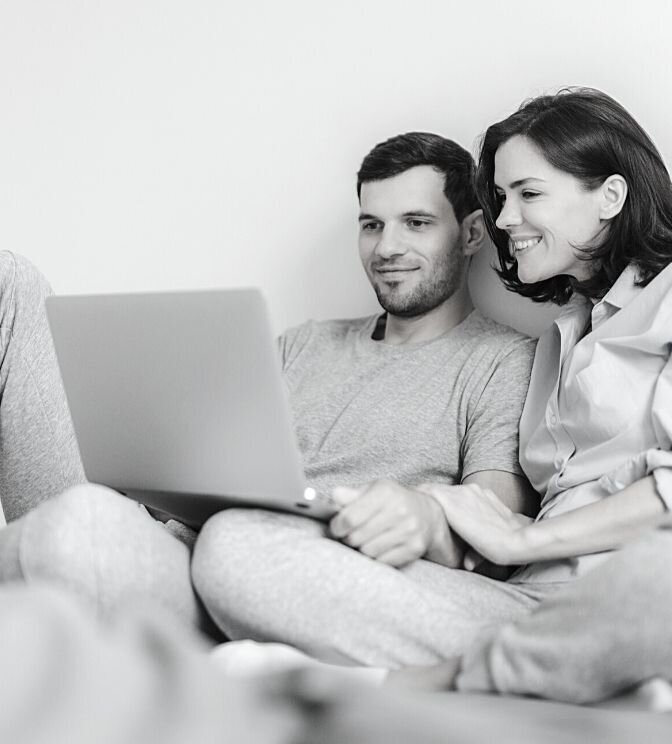 A couple sit against a wall and smile as they watch a laptop screen as a part of their affair recovery program. They appear close and comfortable with one another. This could symbolize their strong bond with one another. We offer support for couples recovering from an affair. Contact us to begin our infidelity recovery program in Miami, FL today.