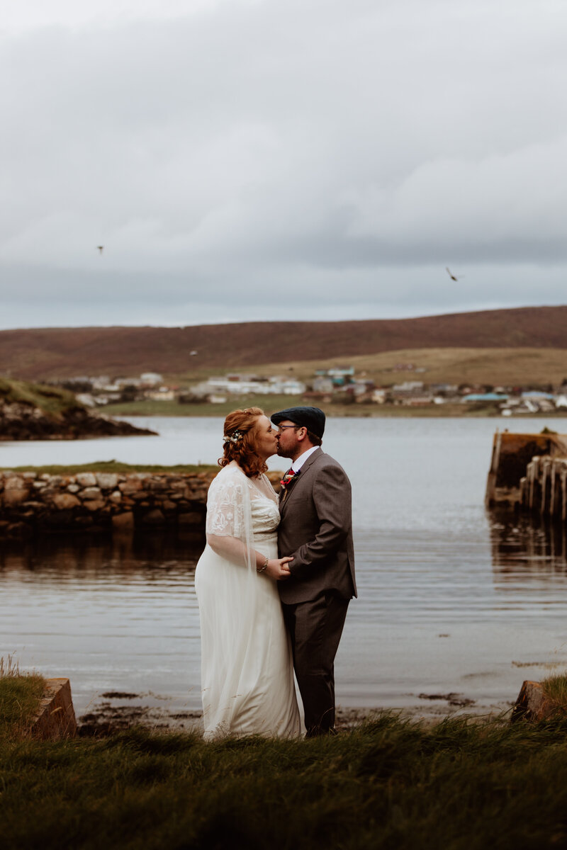 bride and groom kissing at the waters edge