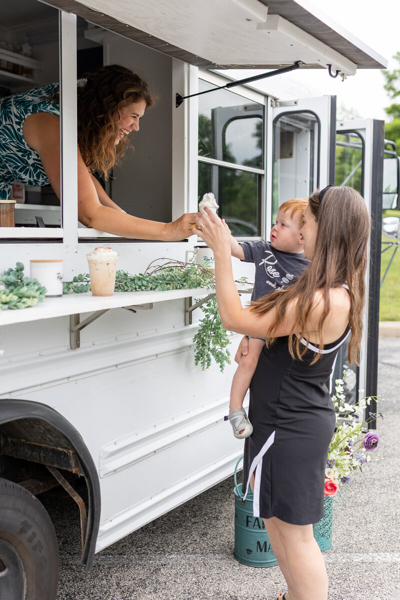 a baby receiving a cup with whipped cream from a coffee truck
