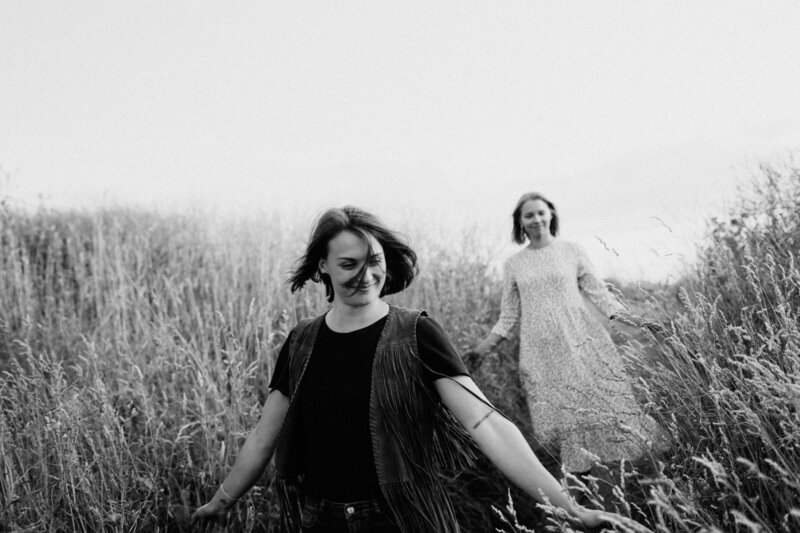 Two adult sisters walking in a field of hay arms stretched in Helsinki in Finland.