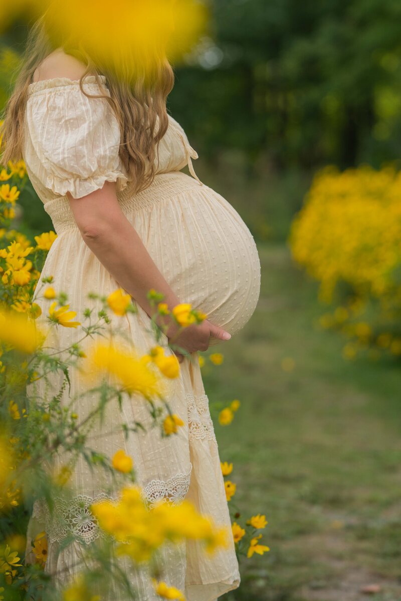 mom hiding behind yellow flowers and holdinger her baby bump at huntington beach ohio