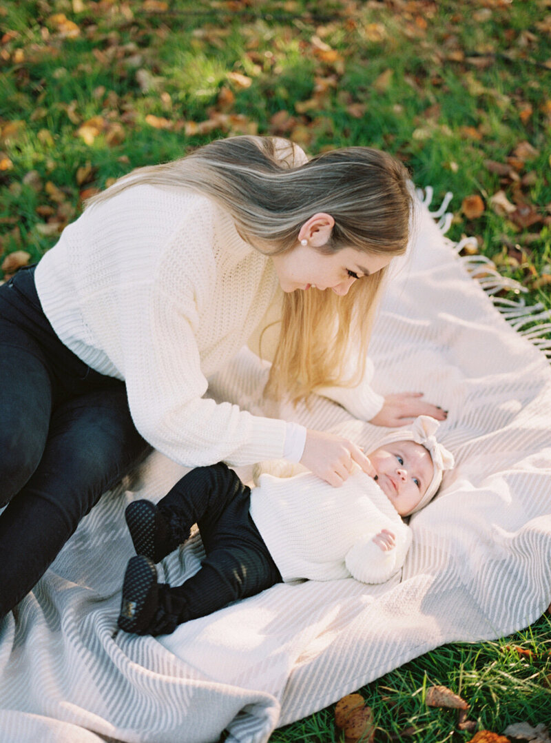 young mum and baby daughter wearing white jumpers on the blanket at park family session