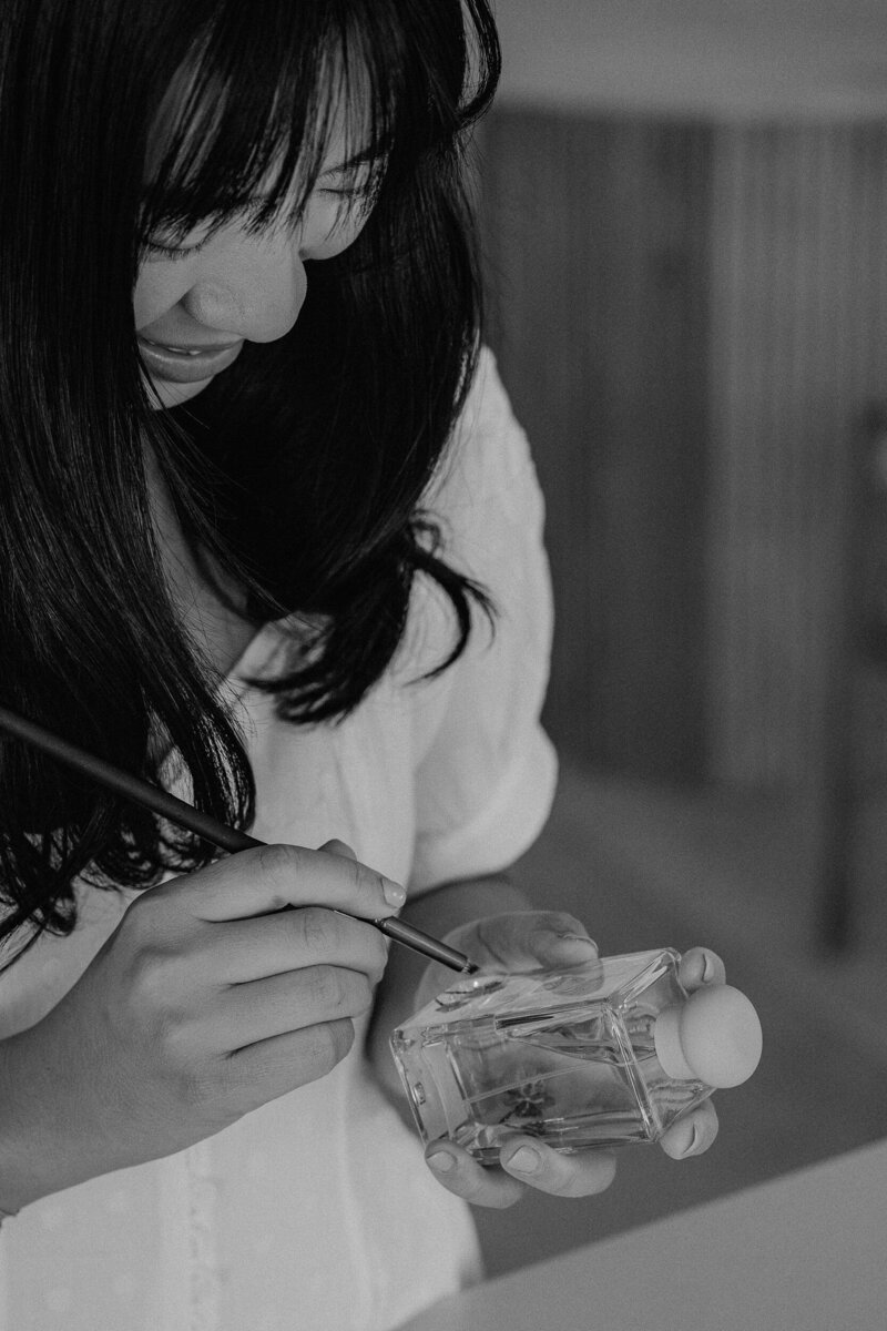 Calligrapher brand photoshoot. Female designer painting on Bvlgari perfume bottle.