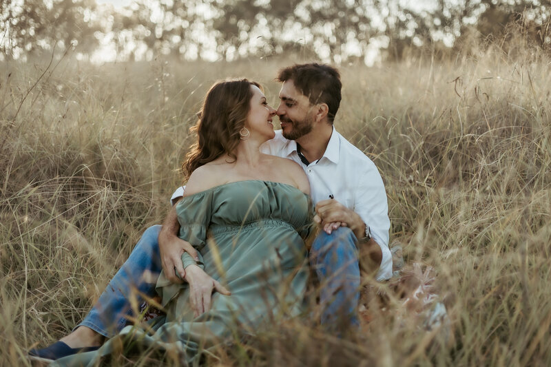 mum and dad to be touching noses in a gorgeous grassy field during their maternity photoshoot