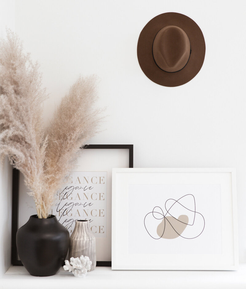 Pictures in frames next to a plant and a hat hanging on the wall.