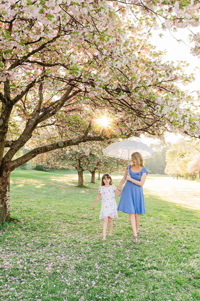 mother and daughter walking under cherry blossom trees in lancaster central park by photographer in york pa