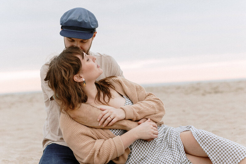 A couple embraces on the beach, with soft waves in the background and a pastel sky during sunset, conveying warmth and intimacy.