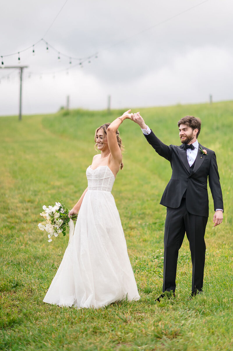 A groom twirling a bride in an open field.
