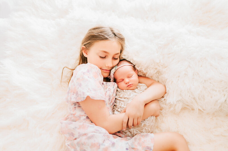 big sister cuddling newborn baby sister in flokati bed captured by Springfield Mo newborn photographer Jessica Kennedy of The XO Photography