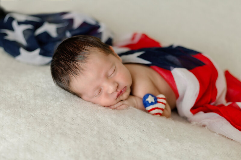 Newborn Photographer, a baby sleeps on the bed wrapped in red white and blue