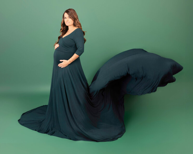 An image from an Orange County Maternity Photographer of a pregnant woman in a red maternity gown standing in a studio holding her bump and smiling up