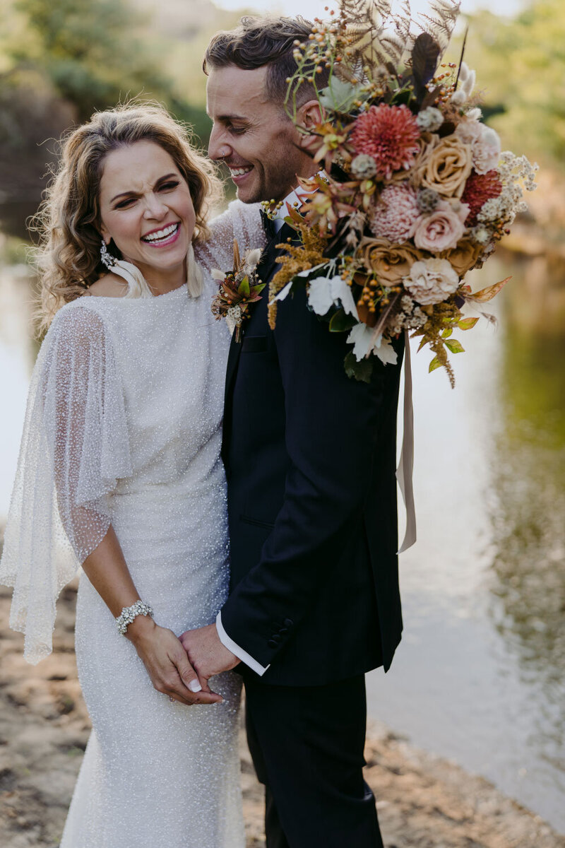 Bride wearing white beaded wedding dress and groom wearing black suit, with dried flower bouquet