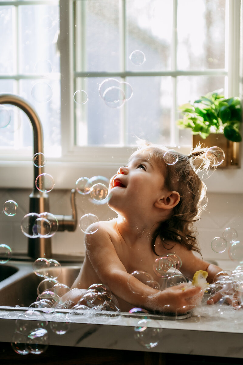 Little girl playing in sink bubbles during an in-home Story of Home session in York, PA.