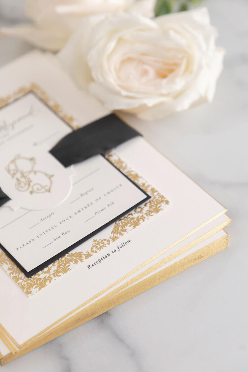 Wedding invitation suite featuring gold foil border, black satin ribbon wrap, and monogrammed response card, designed by Seventh and Anderson.