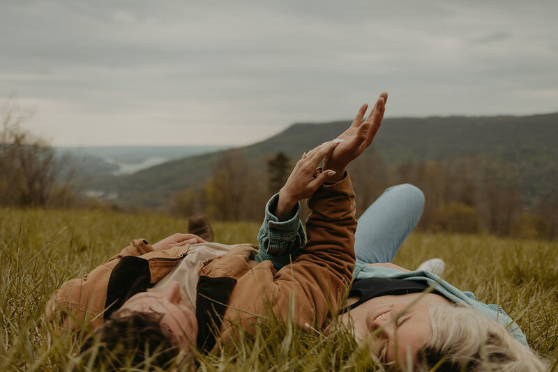 couple laying in grass with mountains in front of them