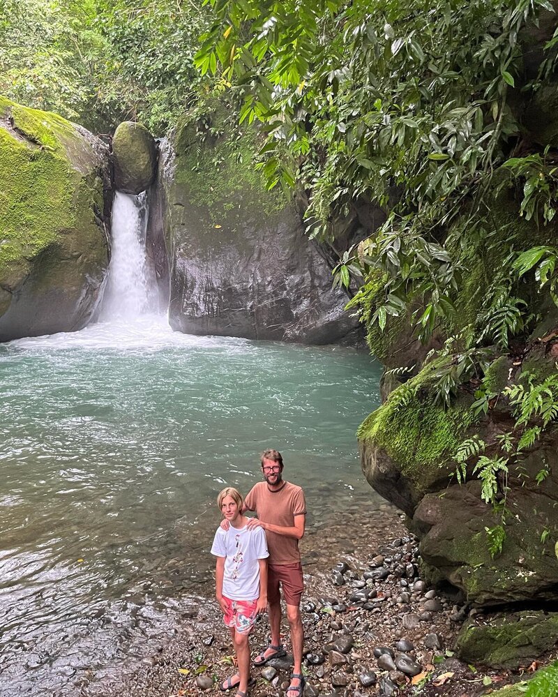 father and son stand at base of waterfall