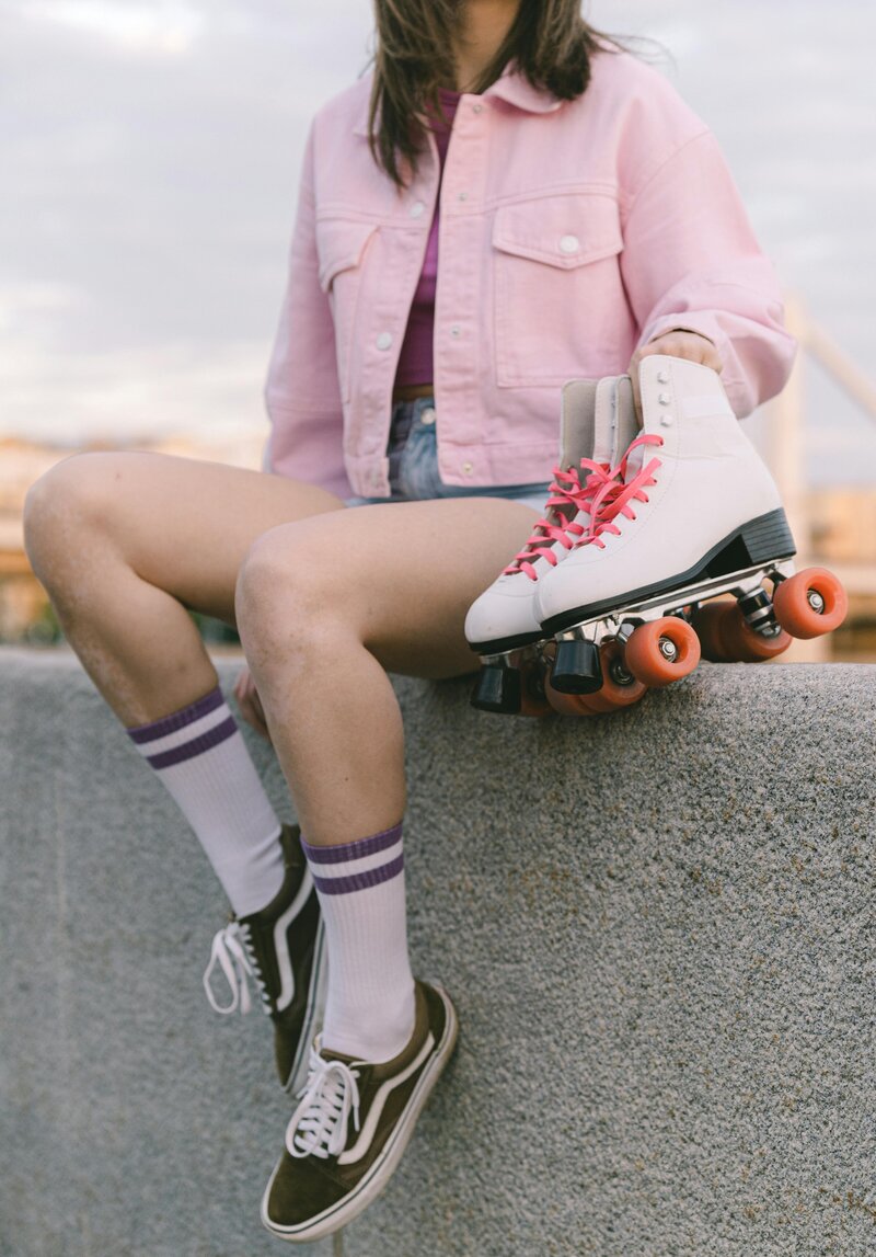 Girl sitting on a wall holds pink roller skates