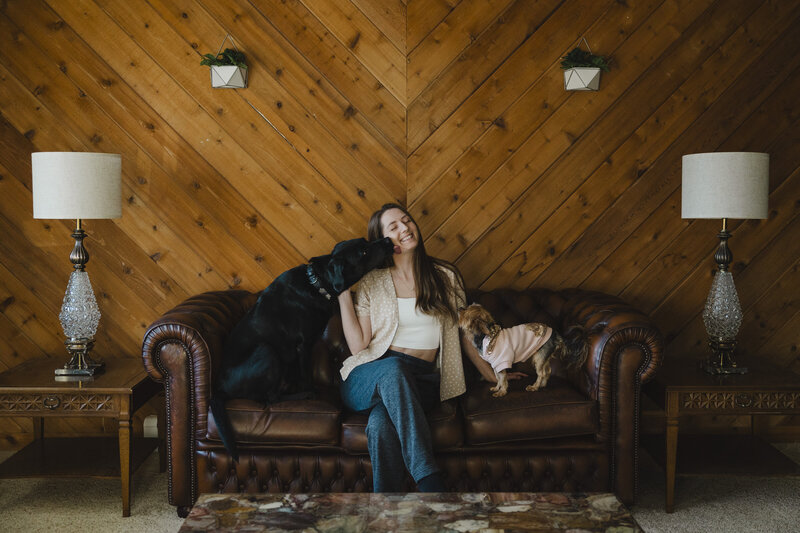 Katie smiles as two dogs give her kisses on a couch.