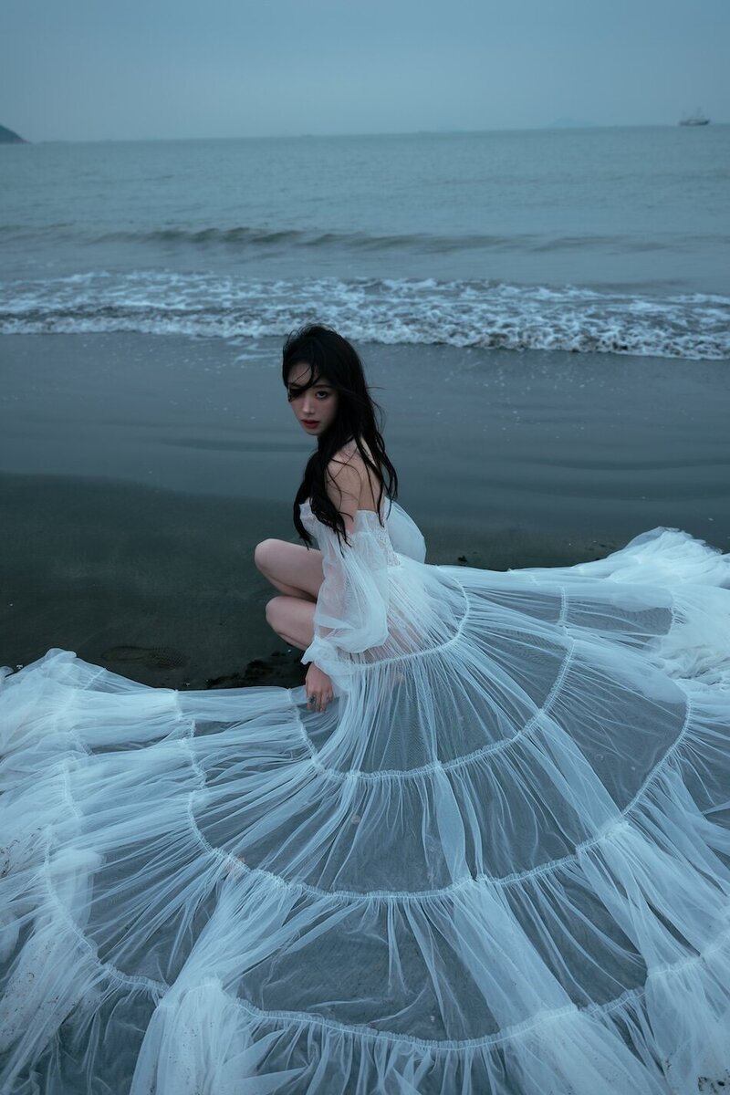 A woman wearing a delicate sheer couture dress shot on the beach in dark moody tones.