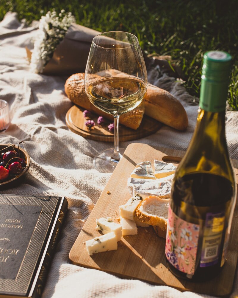 A beautiful picnic spread with wine cheese and bread on a picnic rug.