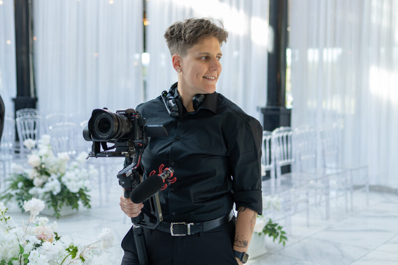 A person in a suit holding a camera and smiling while looking to the side 