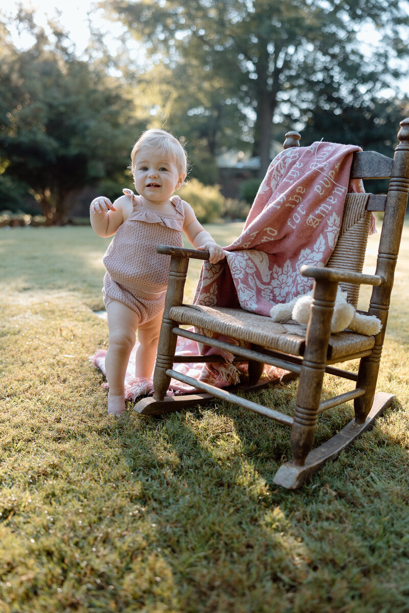 Child stands at a rocking chair and smiles