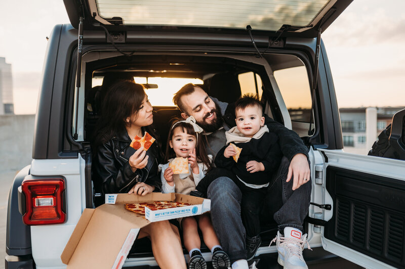 Family eating pizza in their jeep trunk.