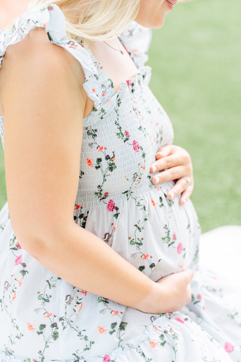 Austin, TX Family & Newborn Photography | An expectant mother sits on a white blanket outside Woodbine Mansion in Round Rock, TX. 