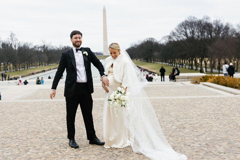 Groom places his hand on his pregnant bride's belly in front of Washington monument