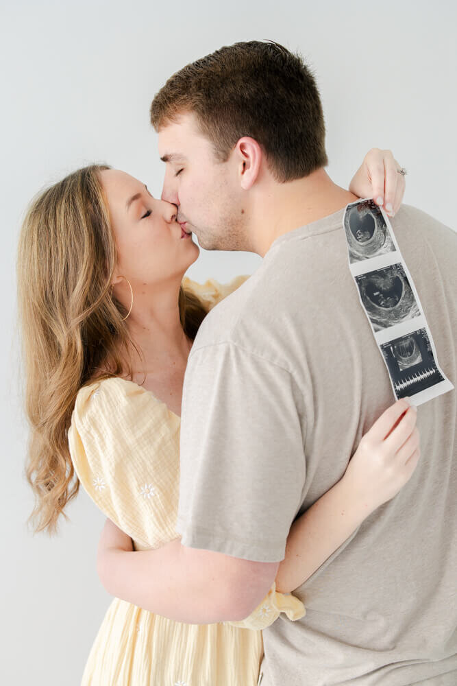 Woman hugging man kissing while holding sonogram to announce pregnancy