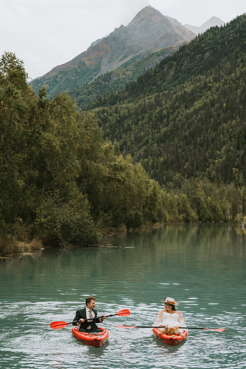couple kayaking in red kayaks at eklutna tailrace in their wedding attire on their elopement day