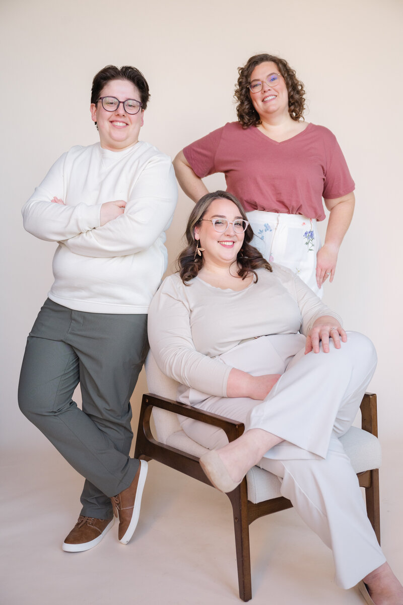 Two people standing next to someone sitting in a chair as they all smile