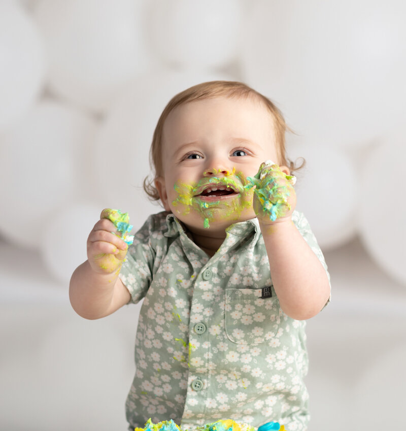 one year old boy eating cake and laughing for first birthday cake smash