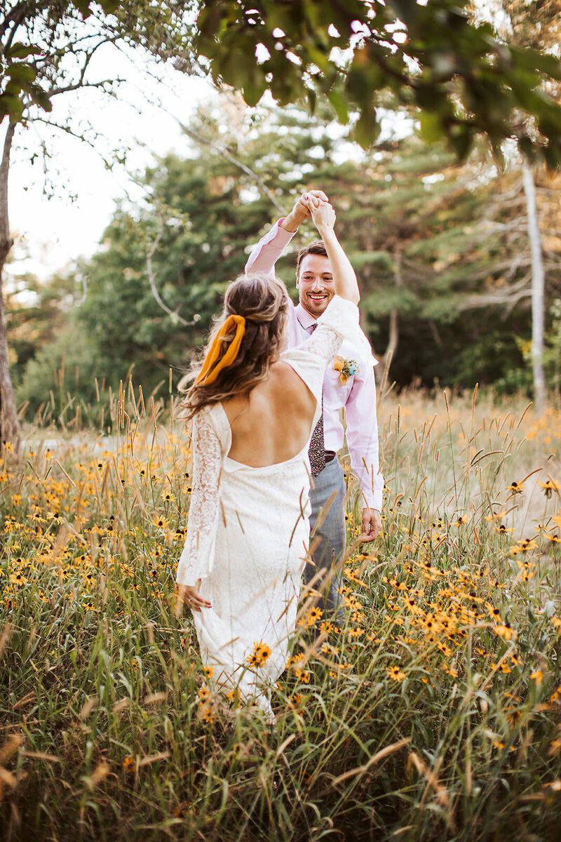 Candid photo of a groom twirling his bride in a wildflower meadow during their Maine elopement.