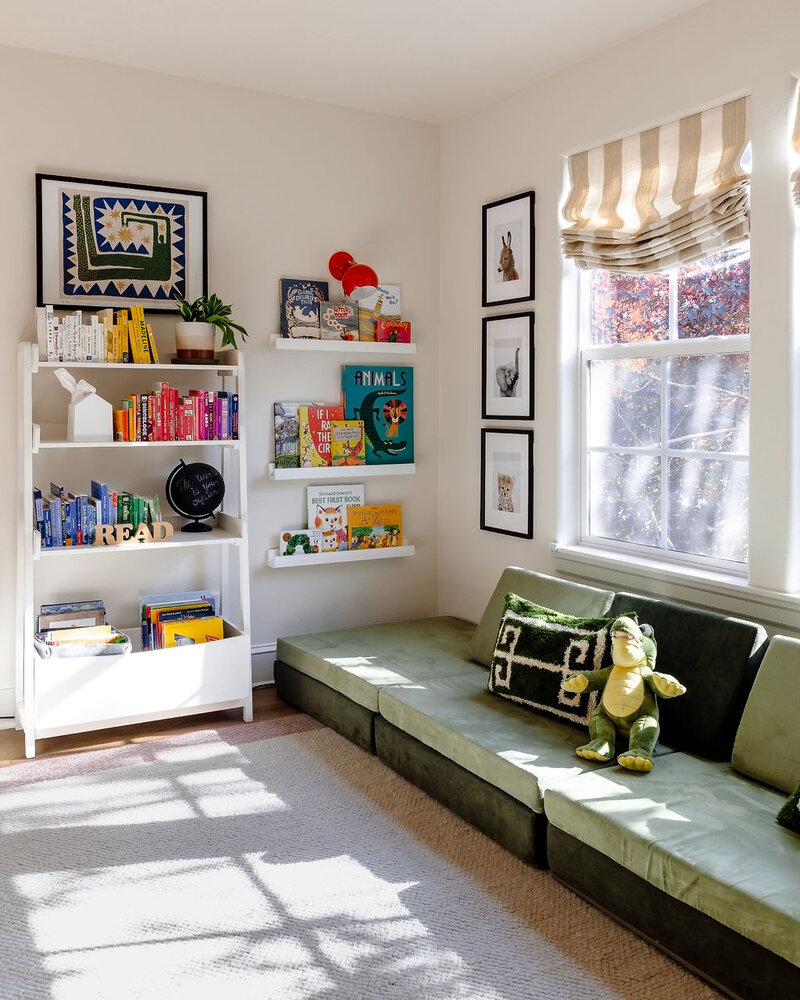 A corner of a kid's area featuring green seating, colorful books on shelves and playful artwork on the wall showcasing colorful home decor.