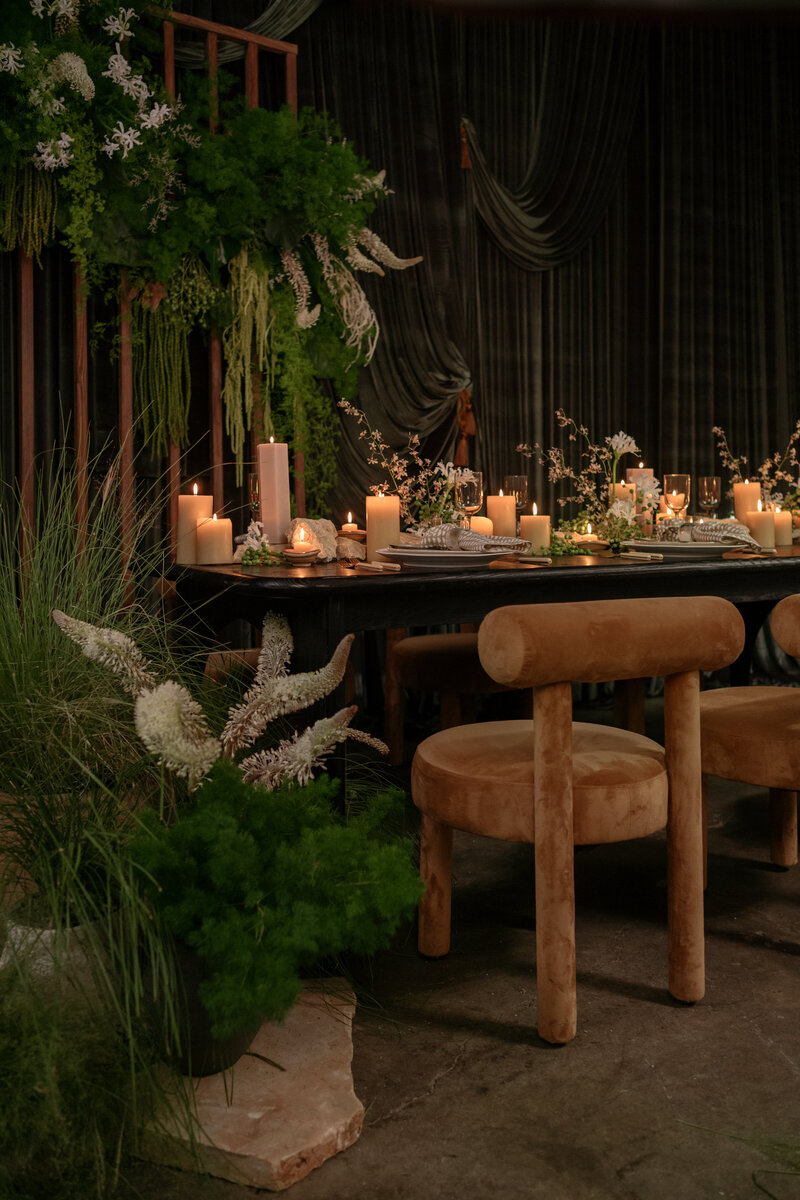 Our cognac bam bam chairs and arches dining table in black with a full tablescape and gorgeous greenery and draping in the background. 