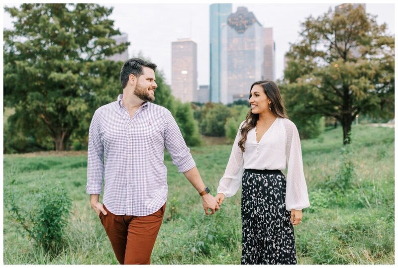 engaged couple in field with Houston skyline