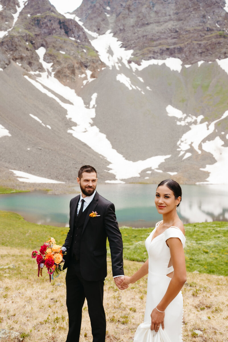 Bride and groom stand in front of a beautiful  blue alpine lake in Ouray Colorado