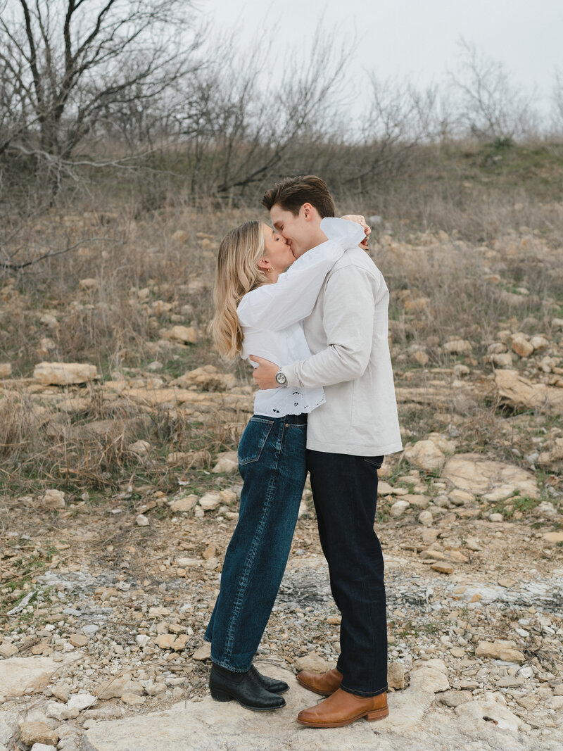 Outdoor image of couple in jeans and boots kissing with their arms wrapped around each other