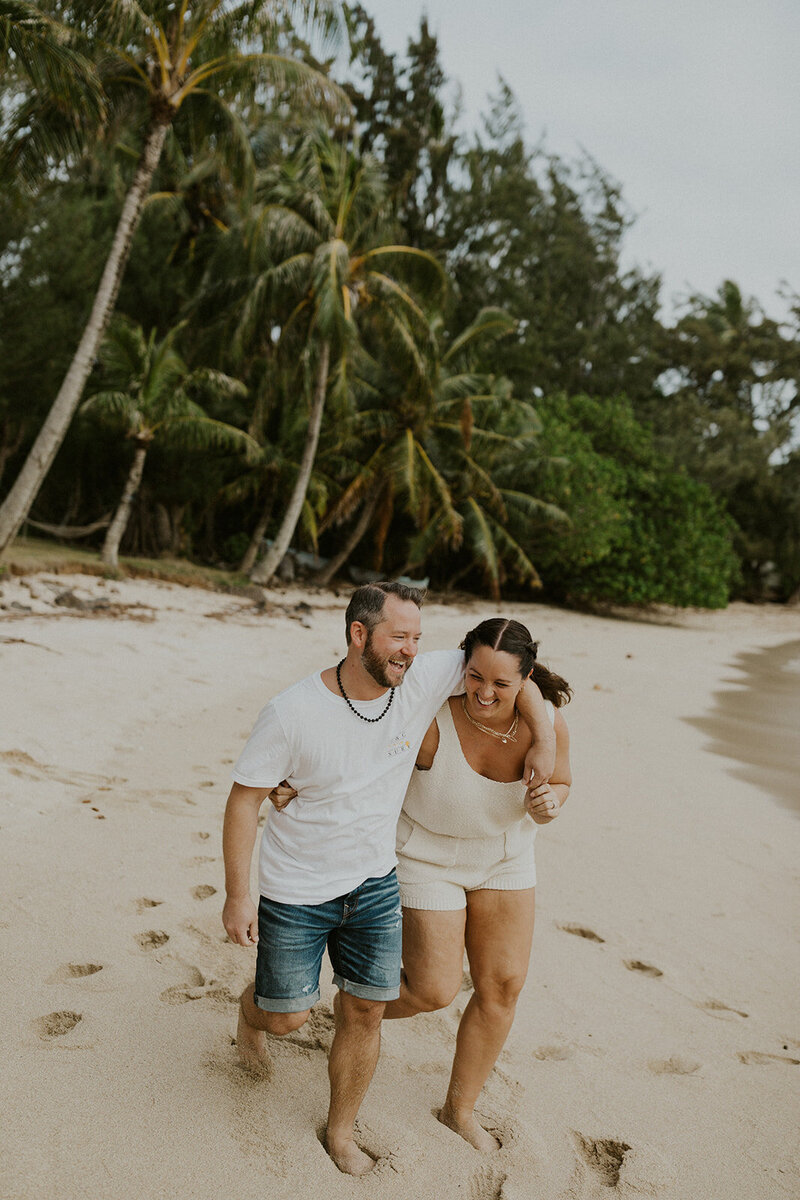 Couple with their arms around each other laughing and walking on a beach