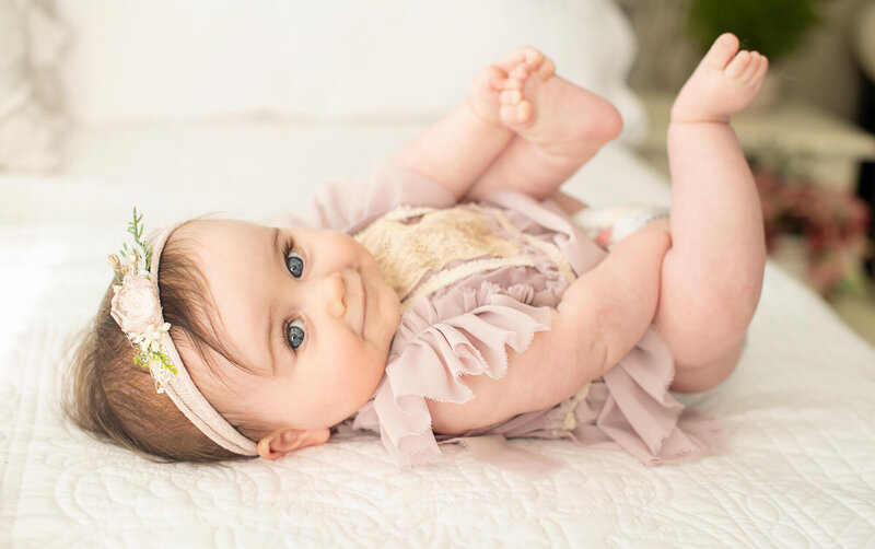 Baby wearing diaper playing with his feet in simple white background