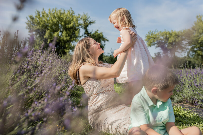 mother hold daughter up and smiles while sitting in a lavender field at lavender lane in milan michigan