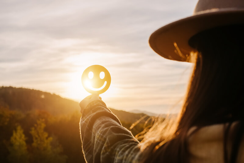 Person holding a smiley face symbol in the sunlight, capturing positivity and encouragement.