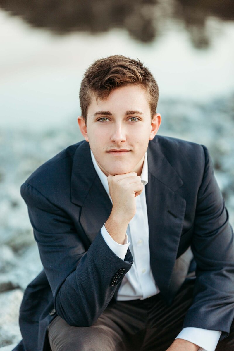A handsome fellow in a suit looking into the camera with a thoughtful gaze during his senior portrait session.