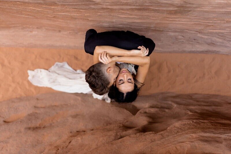 Photo of couple cuddling from a top down view with sand under their feet.