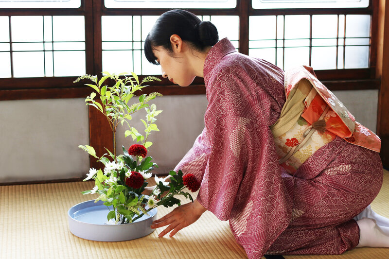 Woman in traditional kimono arranging flowers during a tea ceremony, reflecting cultural immersion and mindful travel experiences.