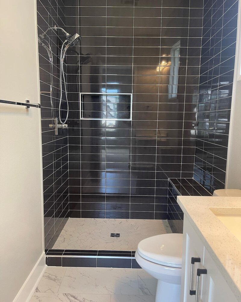 Custom shower with black subway tiles and white grout.