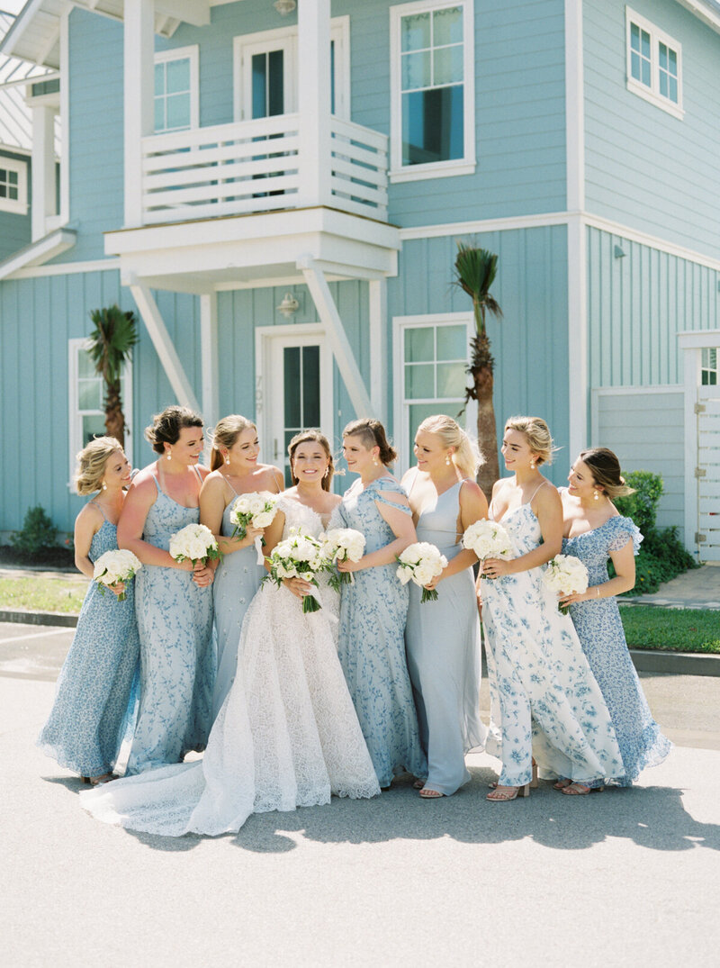 Bridesmaids in mismatched blue dresses with timeless white bouquets at a coastal destination wedding, photographed on film.